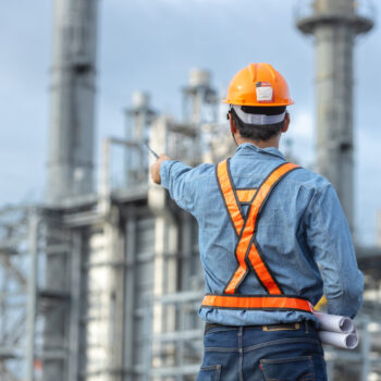 Asian worker power plant factory holding blueprint pointing check construction plan power plant. Engineer wearing safety uniform helmet at energy petrochemical industry.