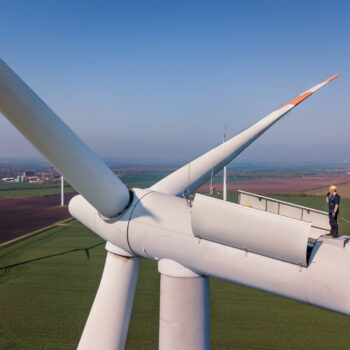 Aerial shot of a worker standing on the top of a wind turbine.