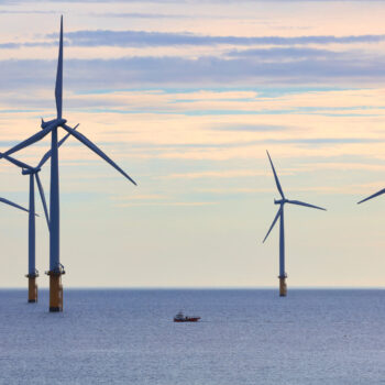 Small Fishing Boat dwarfed by huge Wind Turbines off the North East Coast, Redcar, North Yorkshire, England, UK.
