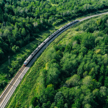 Aerial drone view of train in beautiful green summer forest. Long commuter train moving to railway station