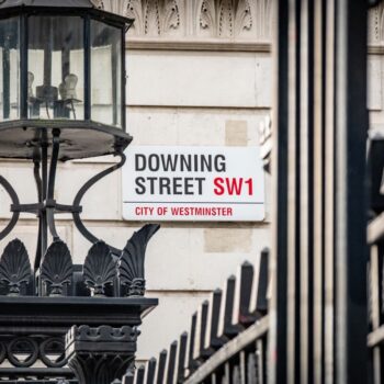 View of the Downing Street sign from the street, with a black lamppost and iron fence.